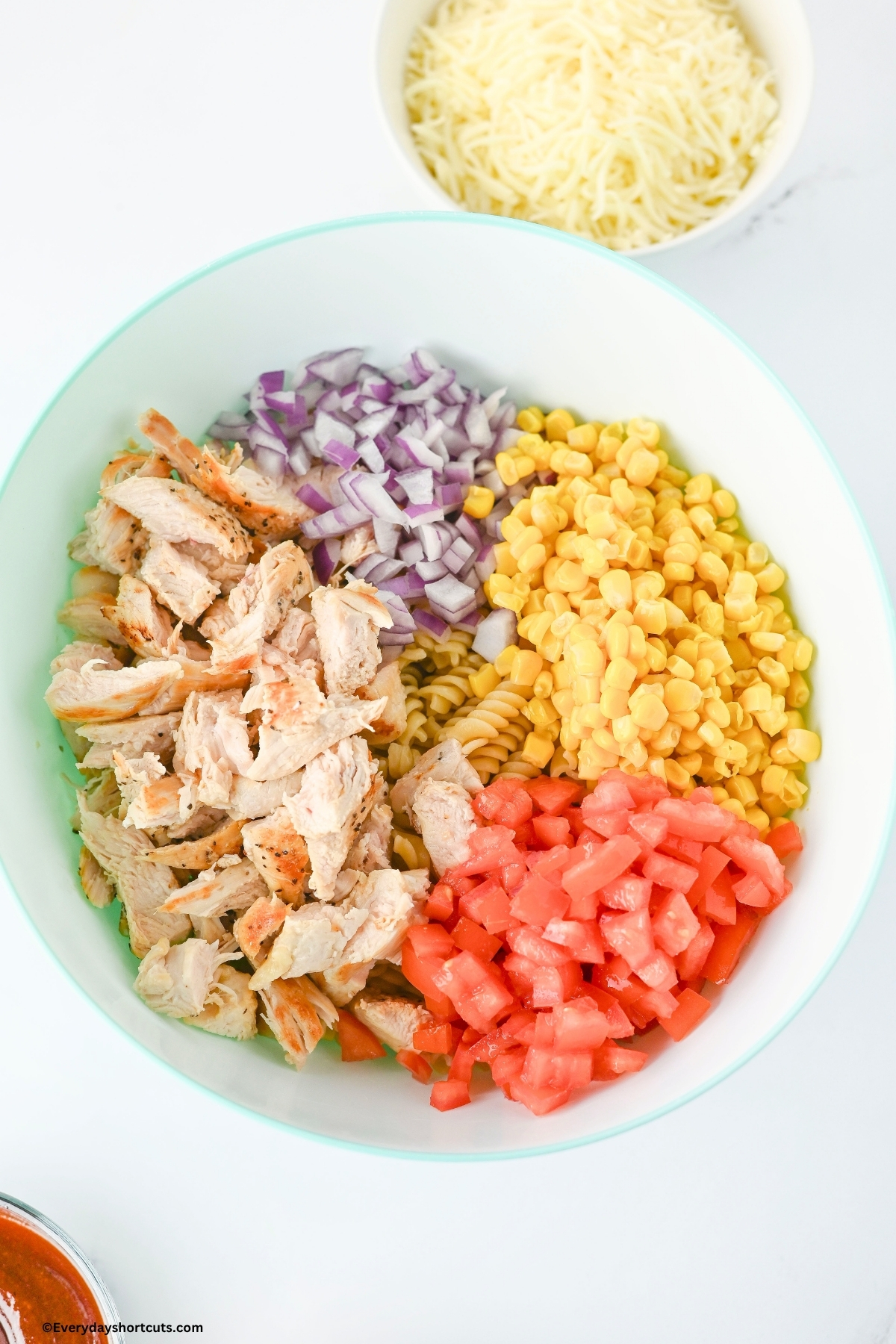 chopped chicken, corn, tomatoes, pasta and red onions in a white bowl