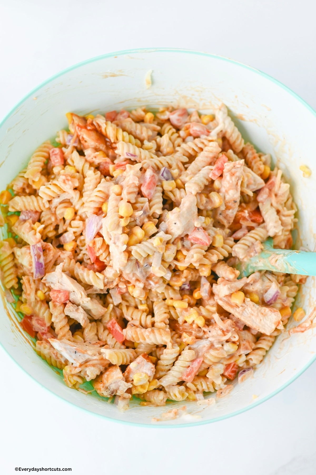 chopped chicken, corn, tomatoes, pasta and red onions in a bowl mixed with BBQ sauce and ranch dressing