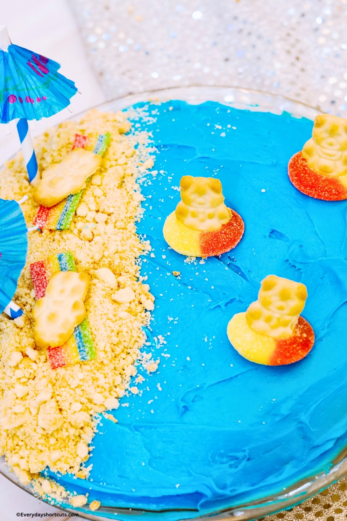 beach cake with sandy beach on one side with cookies and ocean on other half with teddy grahams in peach rings like they are floating in the water