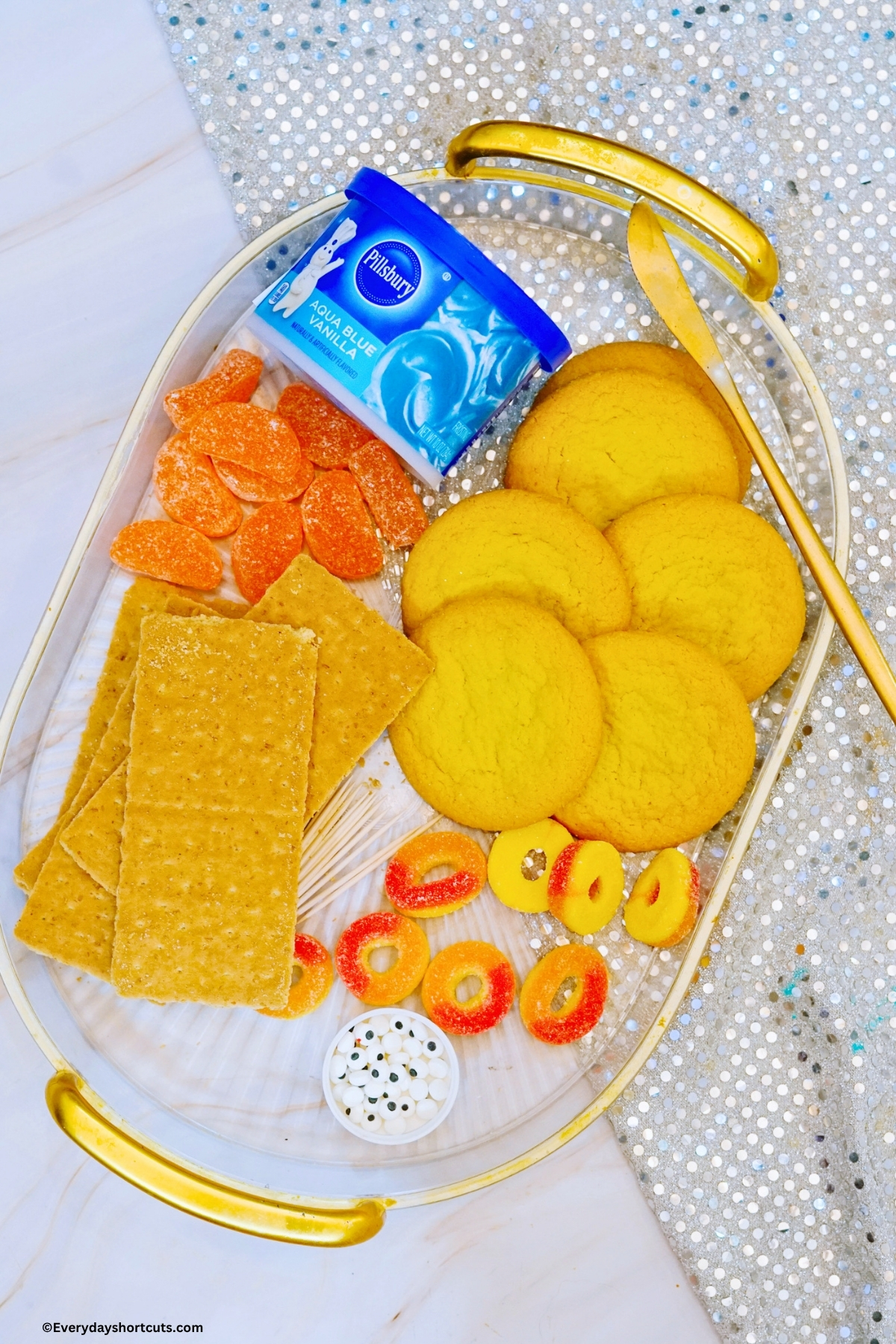 ingredients shown for beach crab cookies: sugar cookies, orange slices, graham crackers, blue frosting, peach rings, candy eyes, toothpicks