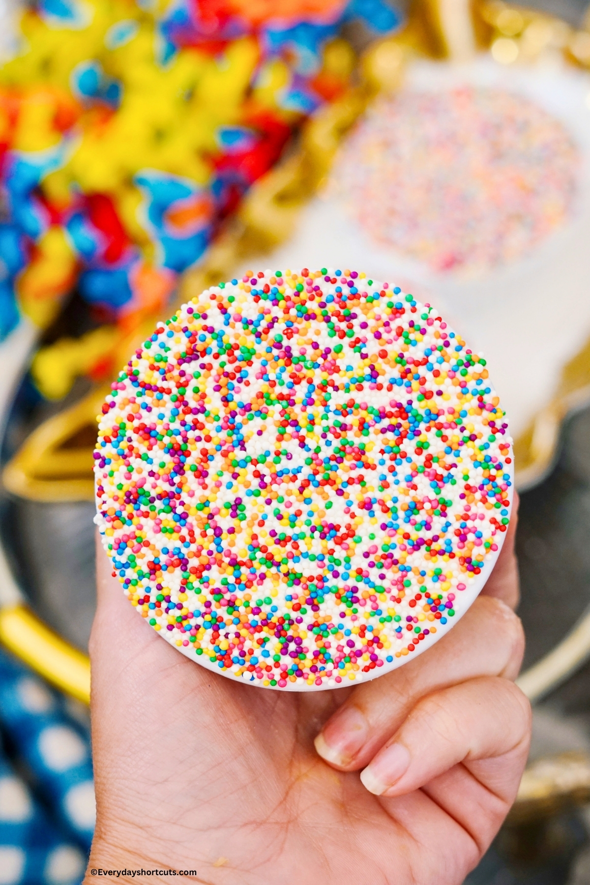 holding a baked yellow cake in ramekin bowl covered in colorful nonpareil sprinkles