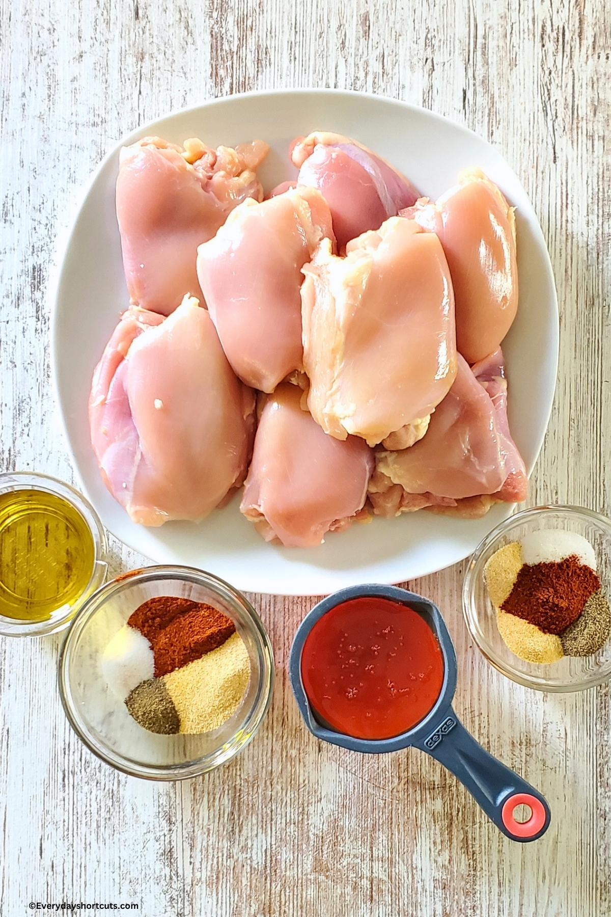 ingredients shown: skinless boneless chicken thighs, olive oil, hot honey, 2 bowls of seasonings consisting of paprika, salt, pepper, and garlic powder