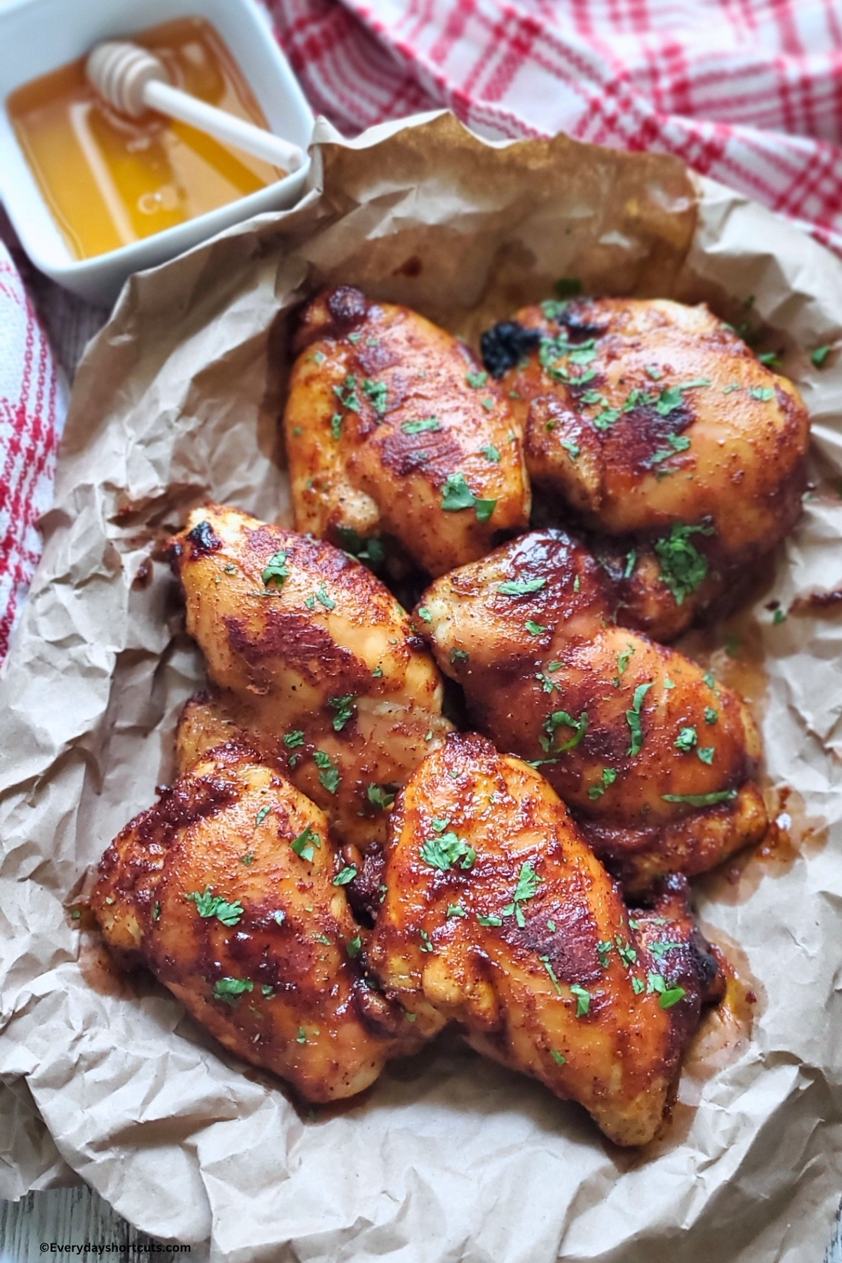 hot honey chicken in a brown paper lined platter next to a bowl of honey with honey stick and red and white striped kitchen towel