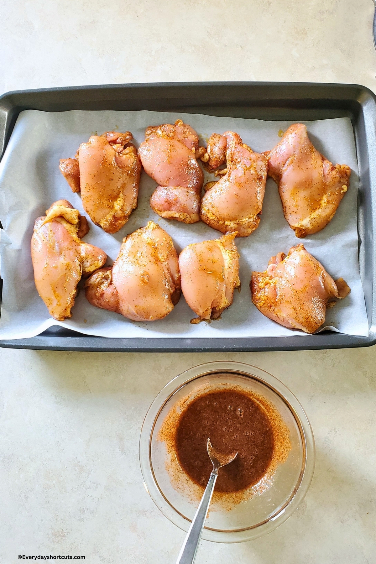 season chicken on a lined with parchment paper cookie sheet next to a bowl of hot honey sauce
