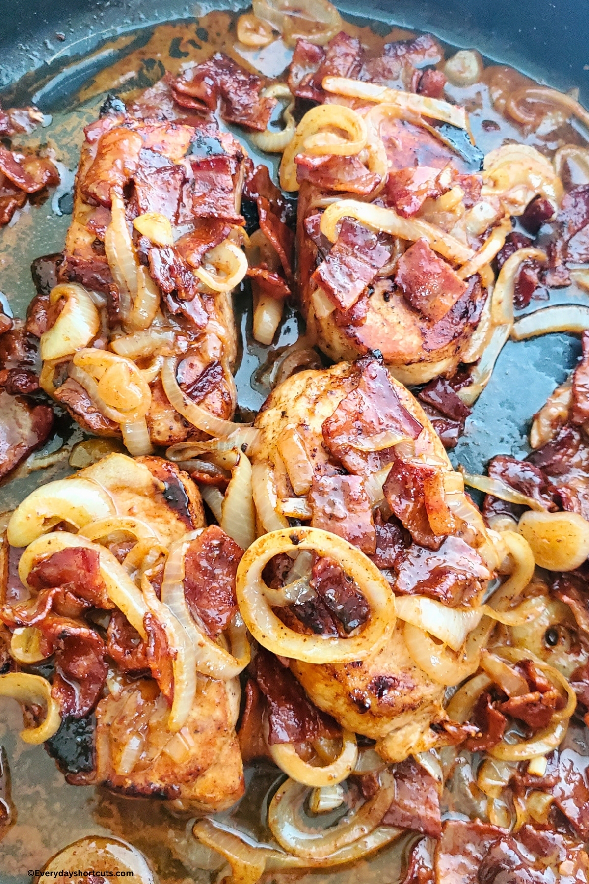 cooked bacon and onions on top of pork chops in a pan
