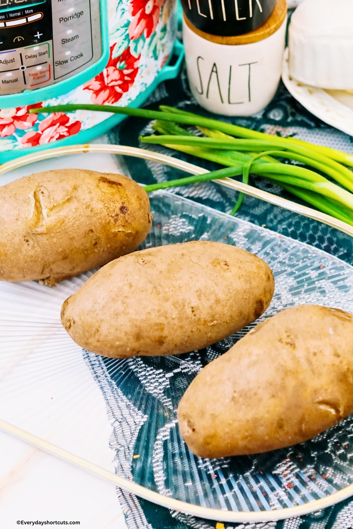 clean potatoes with holes poked in them on a clear tray next to green onions