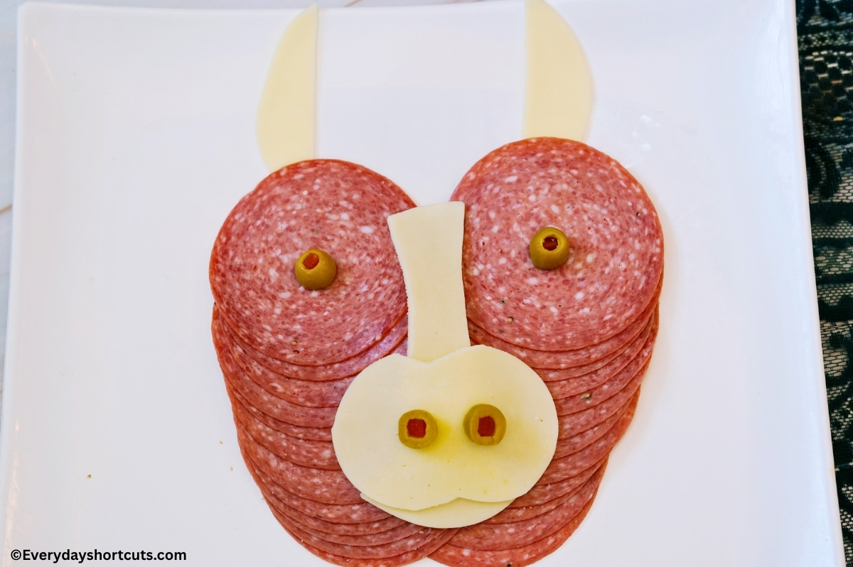 2 rows of overlapping salami next to each other with provolone cheese slices shaped into a nose and horns with green olives for eyes and nostrils