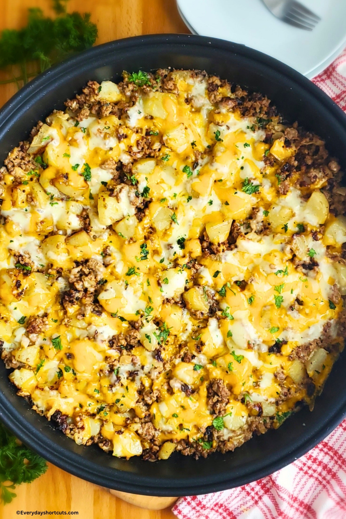 ground beef and potatoes topped with cheese in a skillet next to a white plates and a fork