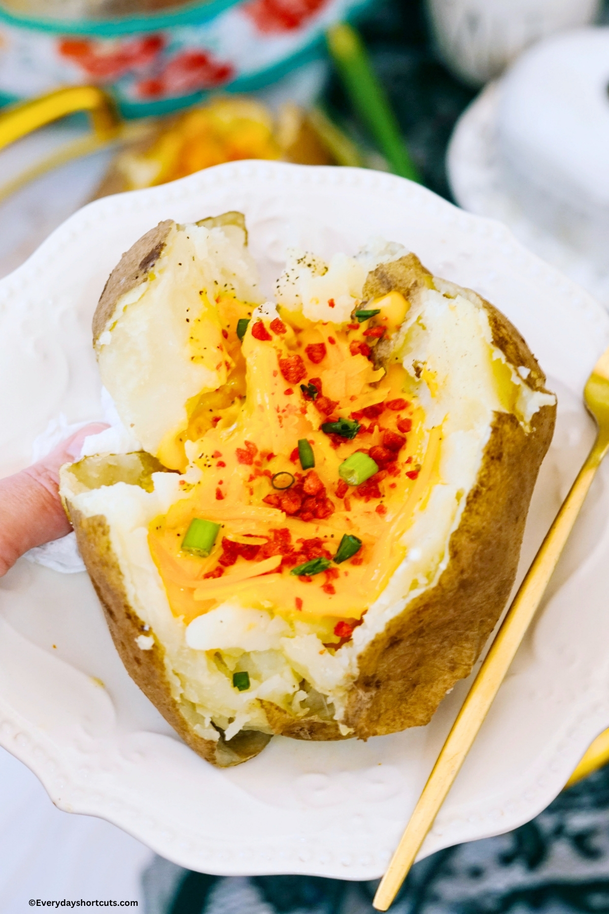 baked potato on a white plate loaded with cheese, bacon bits and green onions