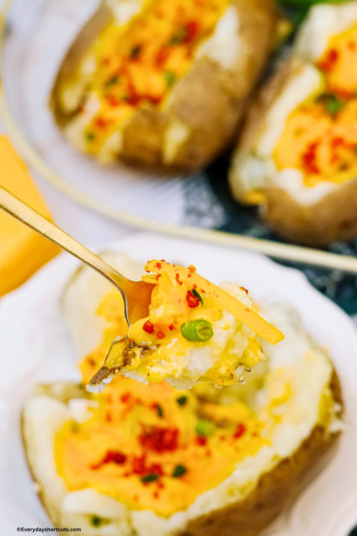 a piece of baked potato with cheese, bacon and green onions on a fork