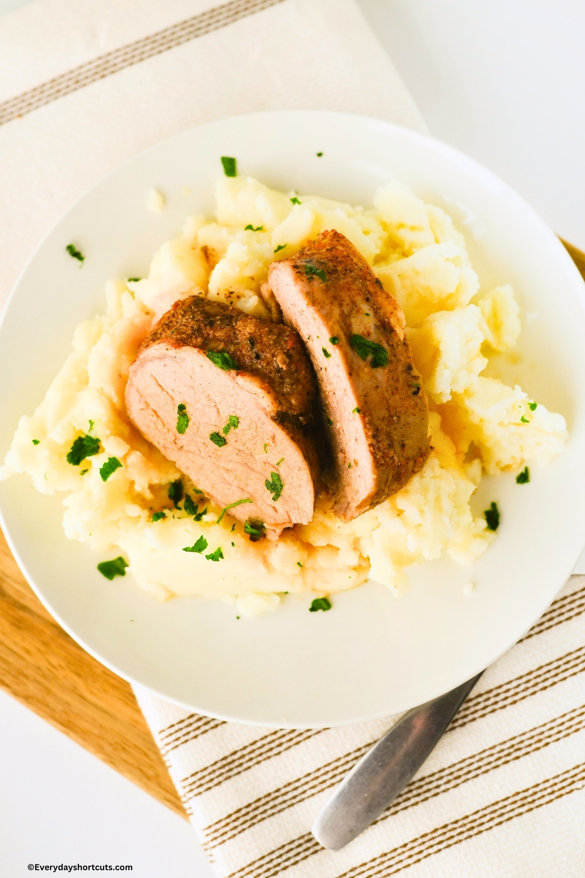 sliced pork tenderloin on a bed of mashed potatoes on a white plate