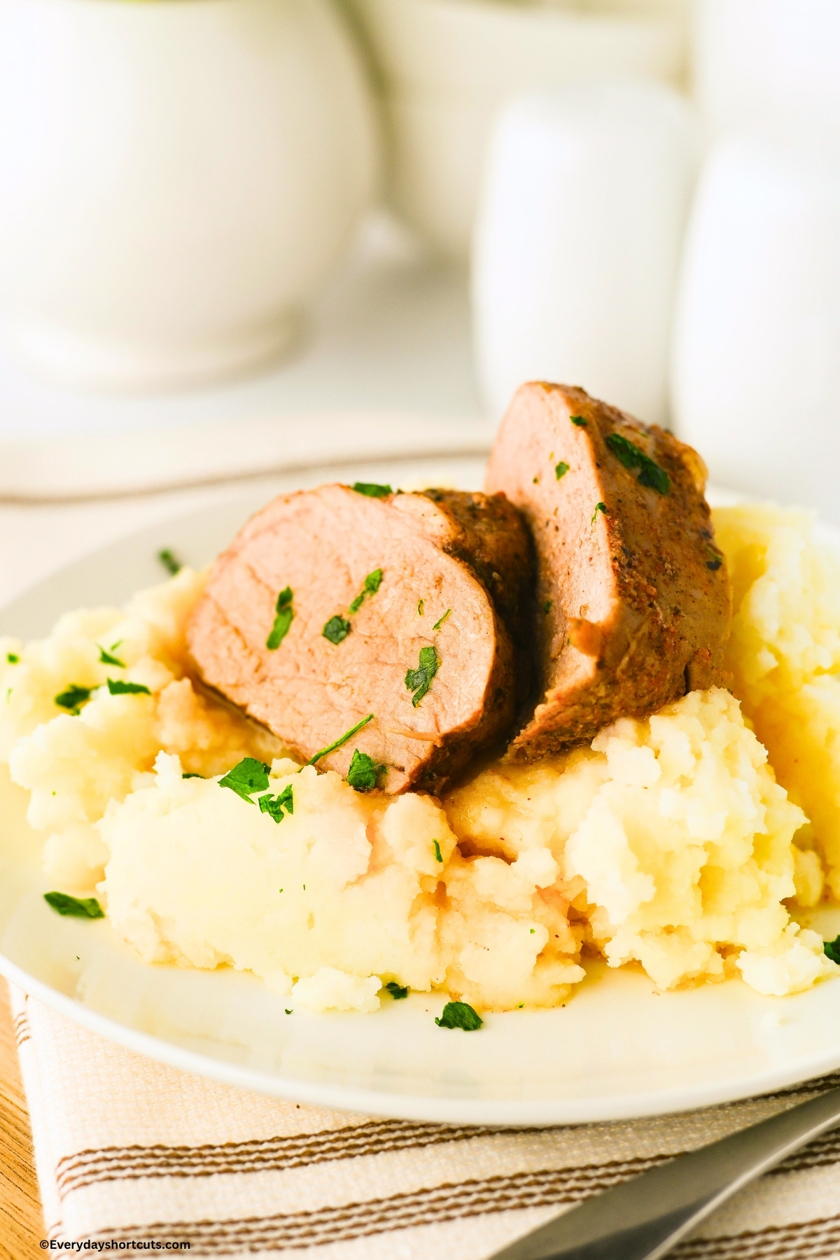 sliced pork on mashed potatoes on a white plate and garnished with parsley