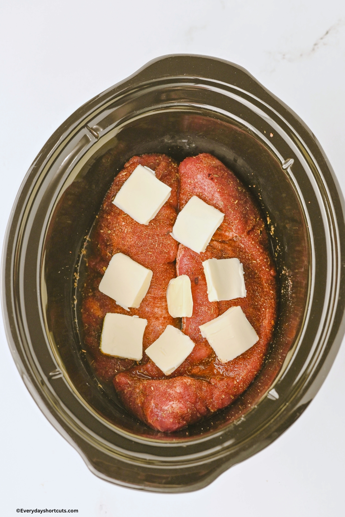2 pork tenderloins in a crockpot with slices of butter on top