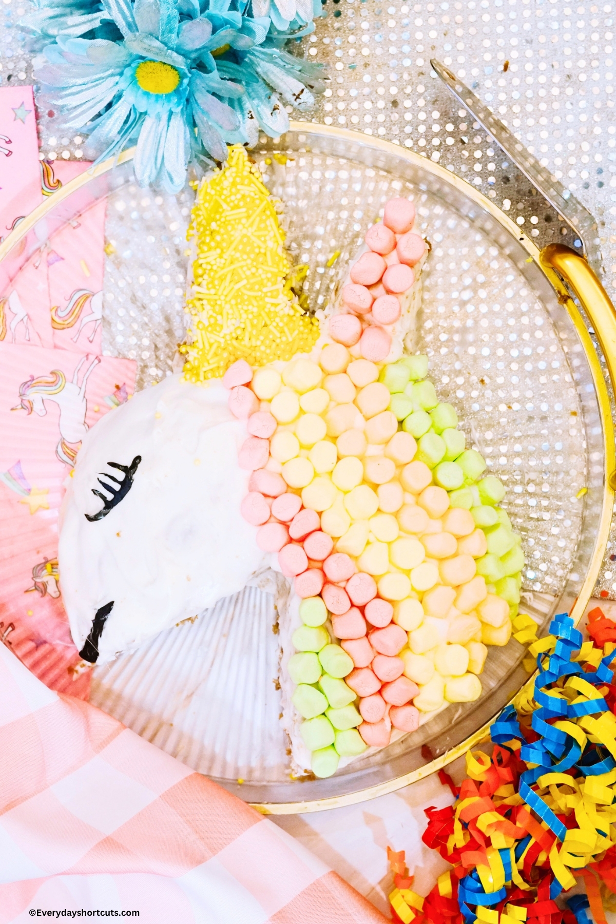 cake decorated to look like a unicorn on a clear tray next to unicorn napkins
