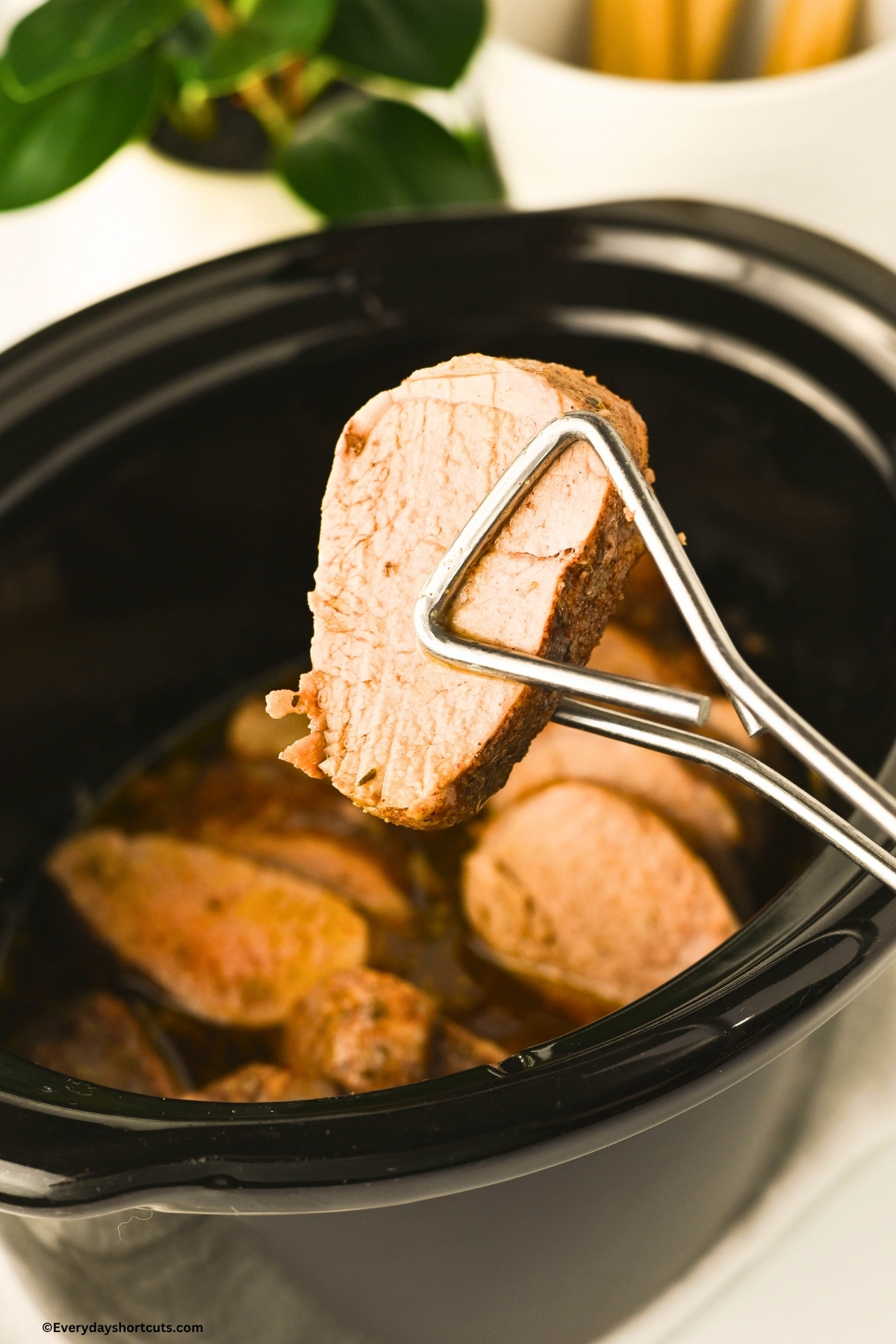 holding a piece of cooked pork tenderloin with tongs