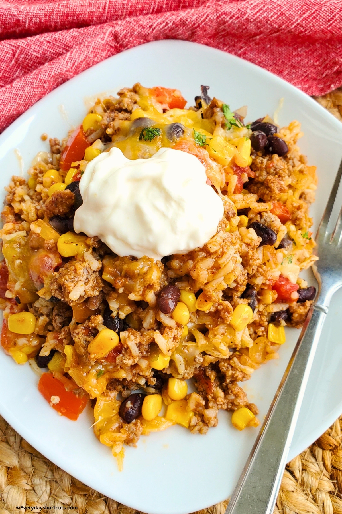 Mexican beef and rice dinner with sour cream on top on a white plate next to a fork