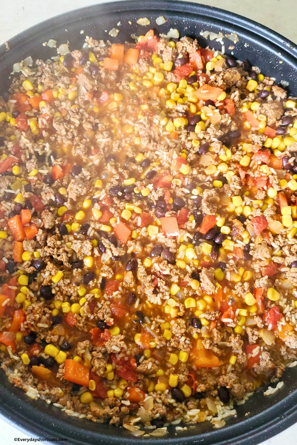 cooked ground beef, tomatoes, rice, corn, black beans, onions and garlic cooked in a skillet