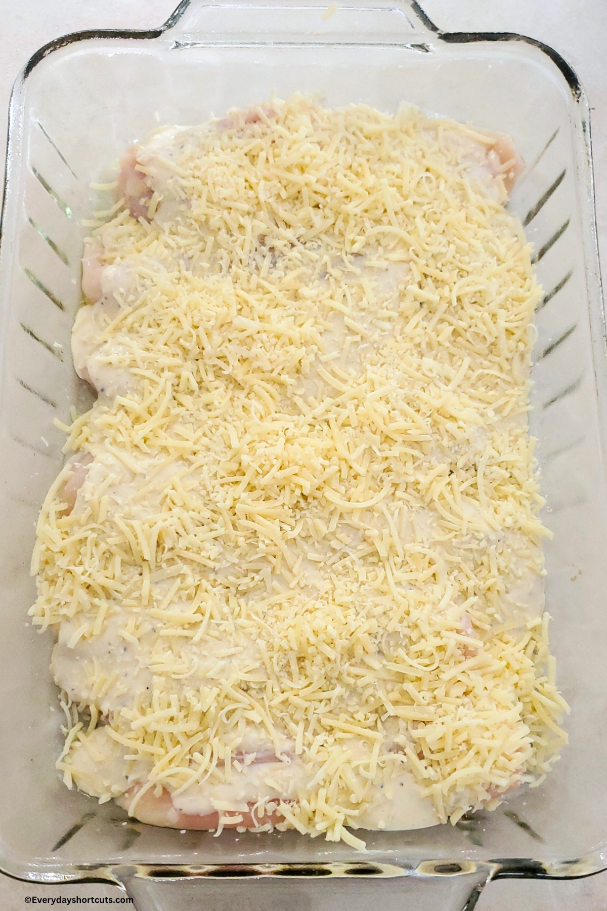 chicken in a casserole dish with Caesar dressing and cheese on top