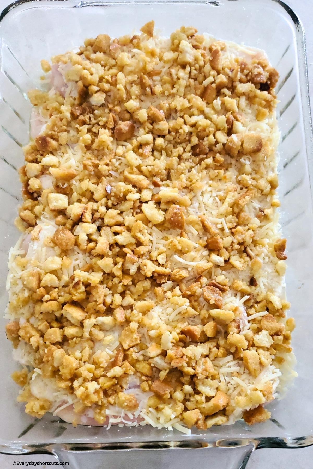 chicken in a casserole dish with Caesar dressing, cheese and crotons on top