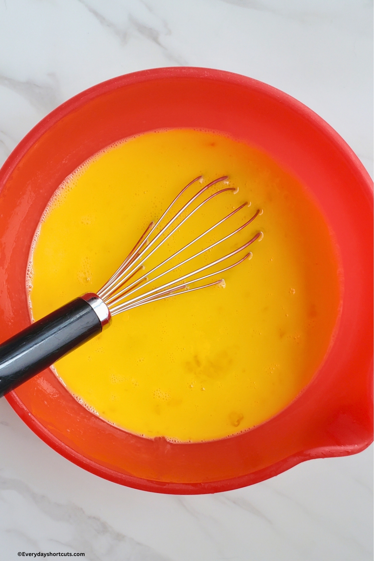 scrambled eggs in a red bowl with a whisk