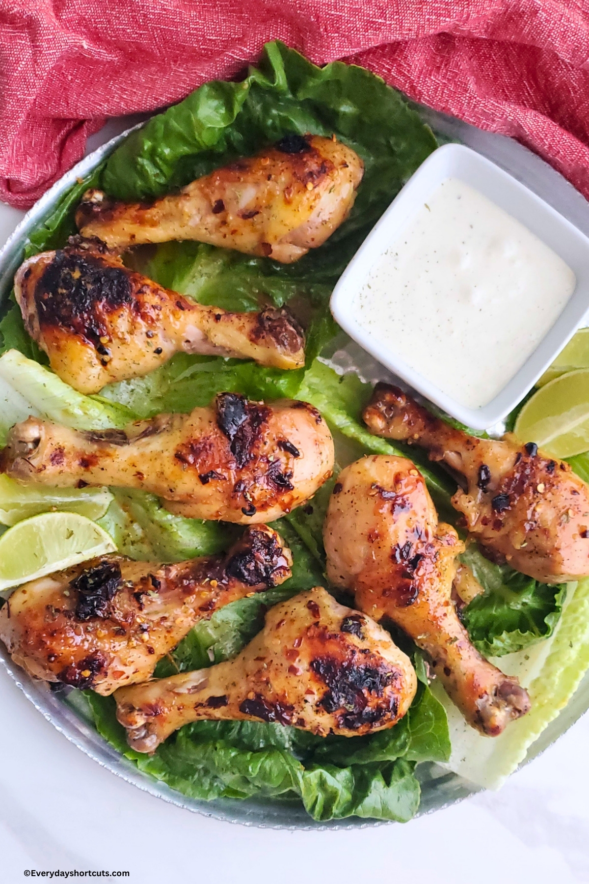 chicken drumsticks with firecracker sauce on top on a lettuce bed next to limes and ranch dressing in a bowl
