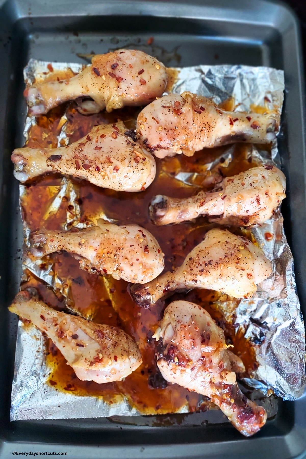chicken drumsticks on a baking sheet with firecracker sauce poured over top