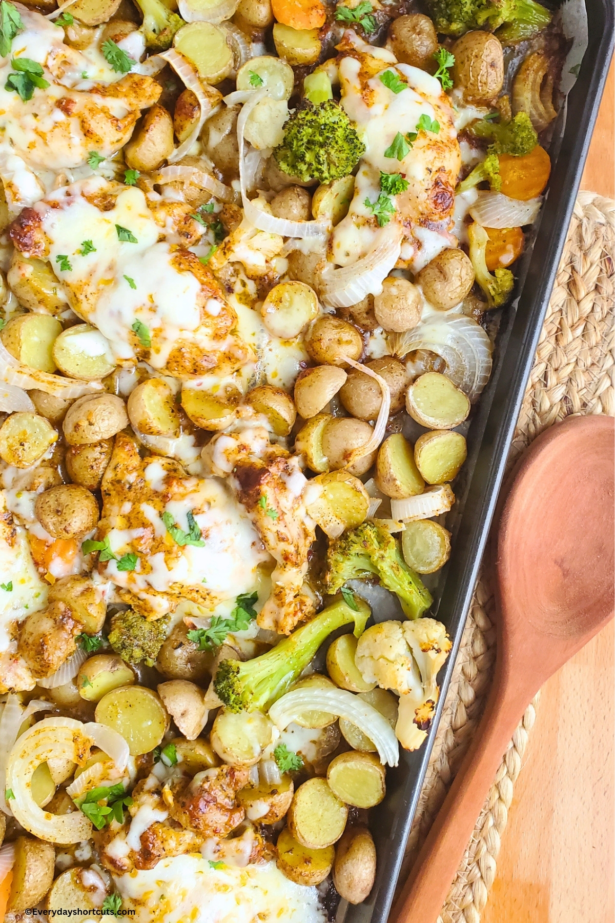 up close of garlic parmesan chicken thighs on a sheet pan with potatoes and veggies next to a wooden spoon
