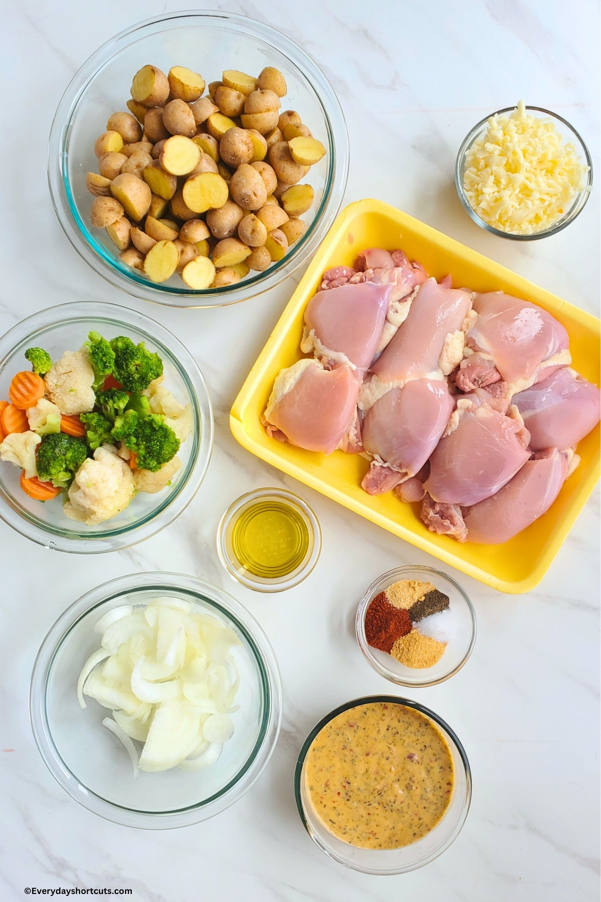 ingredients shown: chicken thighs, shredded parmesan cheese, baby potatoes, mixed vegetables, olive oil, onions, parmesan garlic sauce, salt, pepper, paprika, garlic powder, onion powder