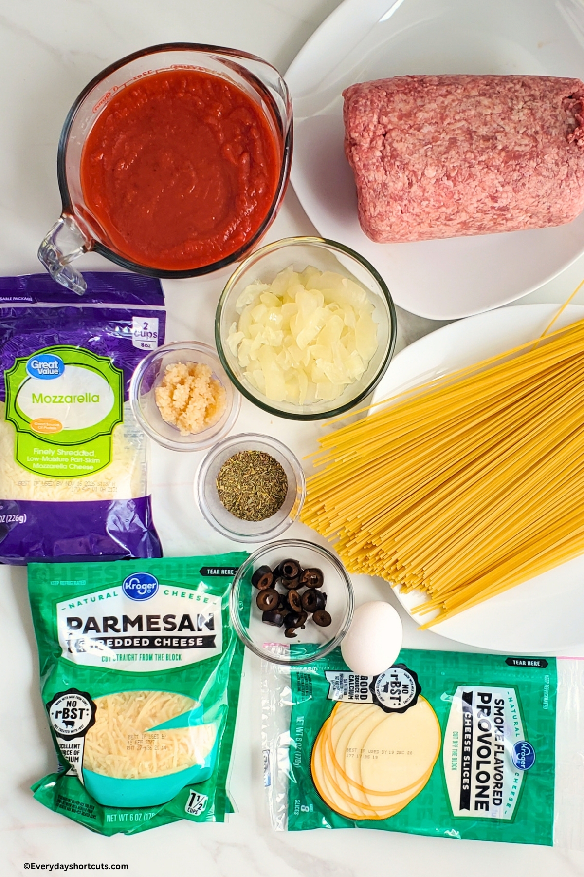ingredients shown: ground beef, marinara sauce, onions, minced garlic, spaghetti, Italian seasoning, egg, black olives, provolone cheese slices, mozzarella and parmesan shredded cheese