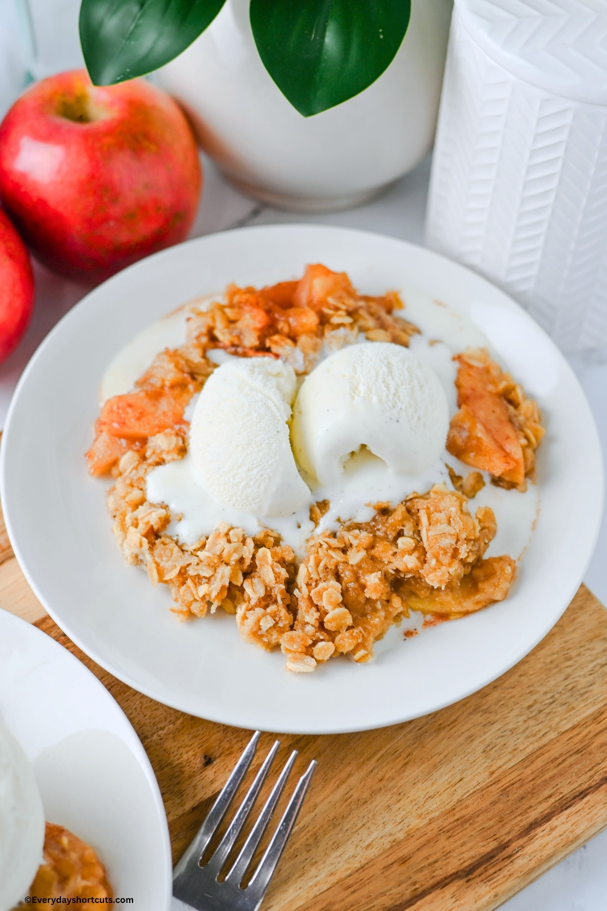 apple crisp on a white plate with a scoop of ice cream next to apples