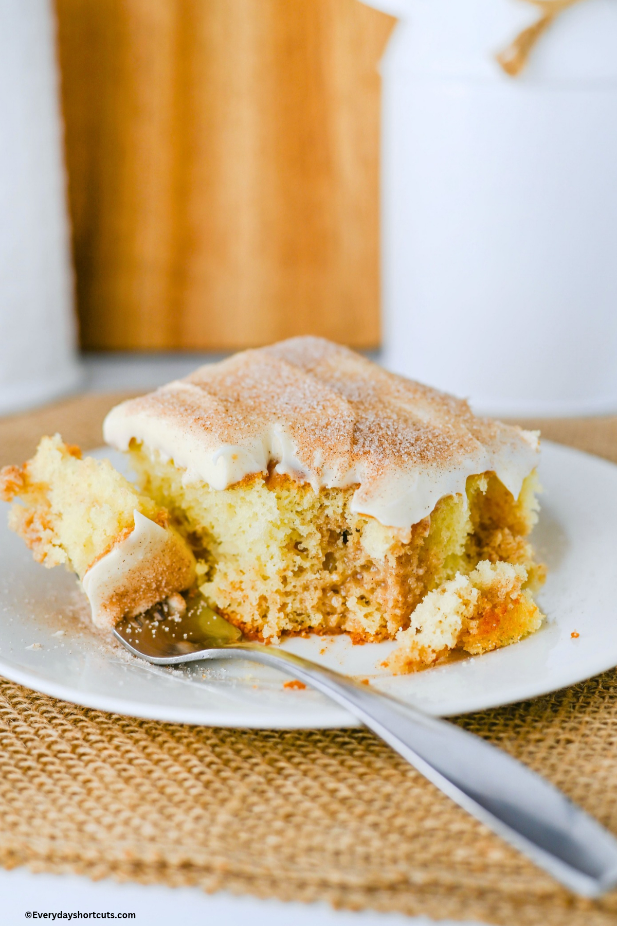 fork with a piece of cinnamon roll poke cake on it next to a slice of cake on a white plate