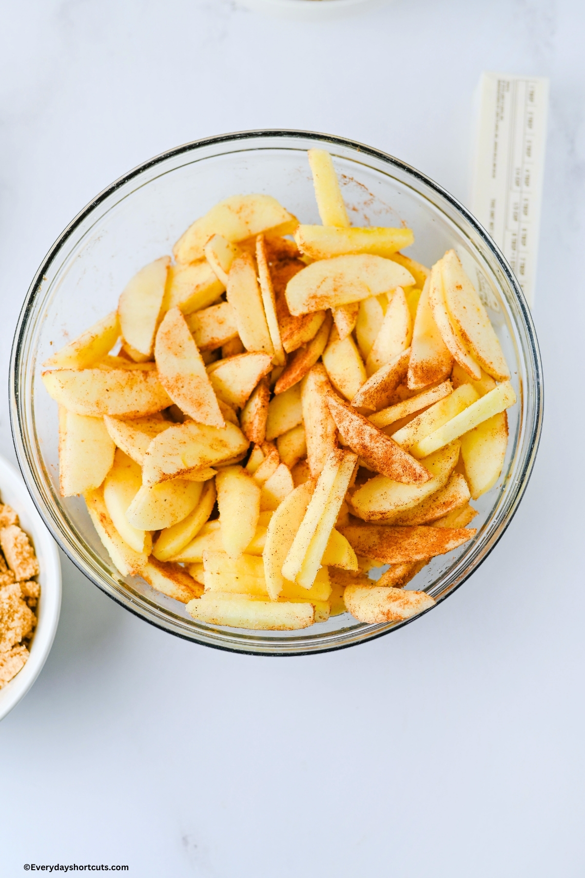 peeled and sliced apples with sugar, cinnamon and nutmeg on top in a bowl