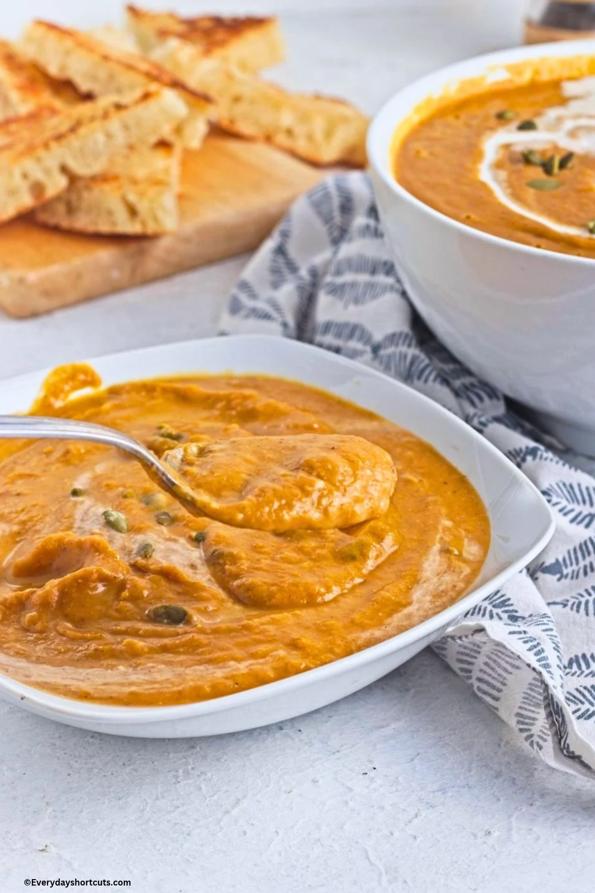 bowl of pumpkin soup with a spoonful of pumpkin soup next to a blue and white napkin