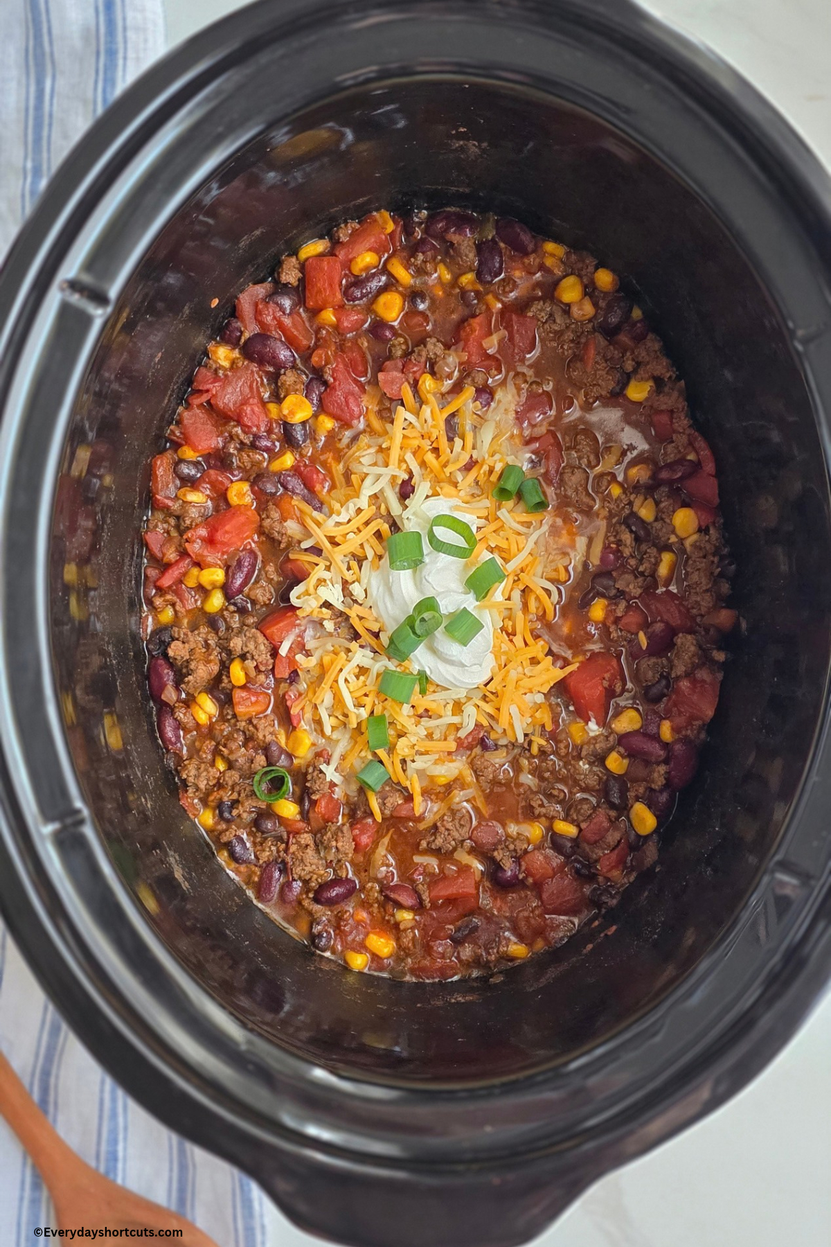 cooked taco soup in crockpot with shredded cheese, green onions and sour cream on top