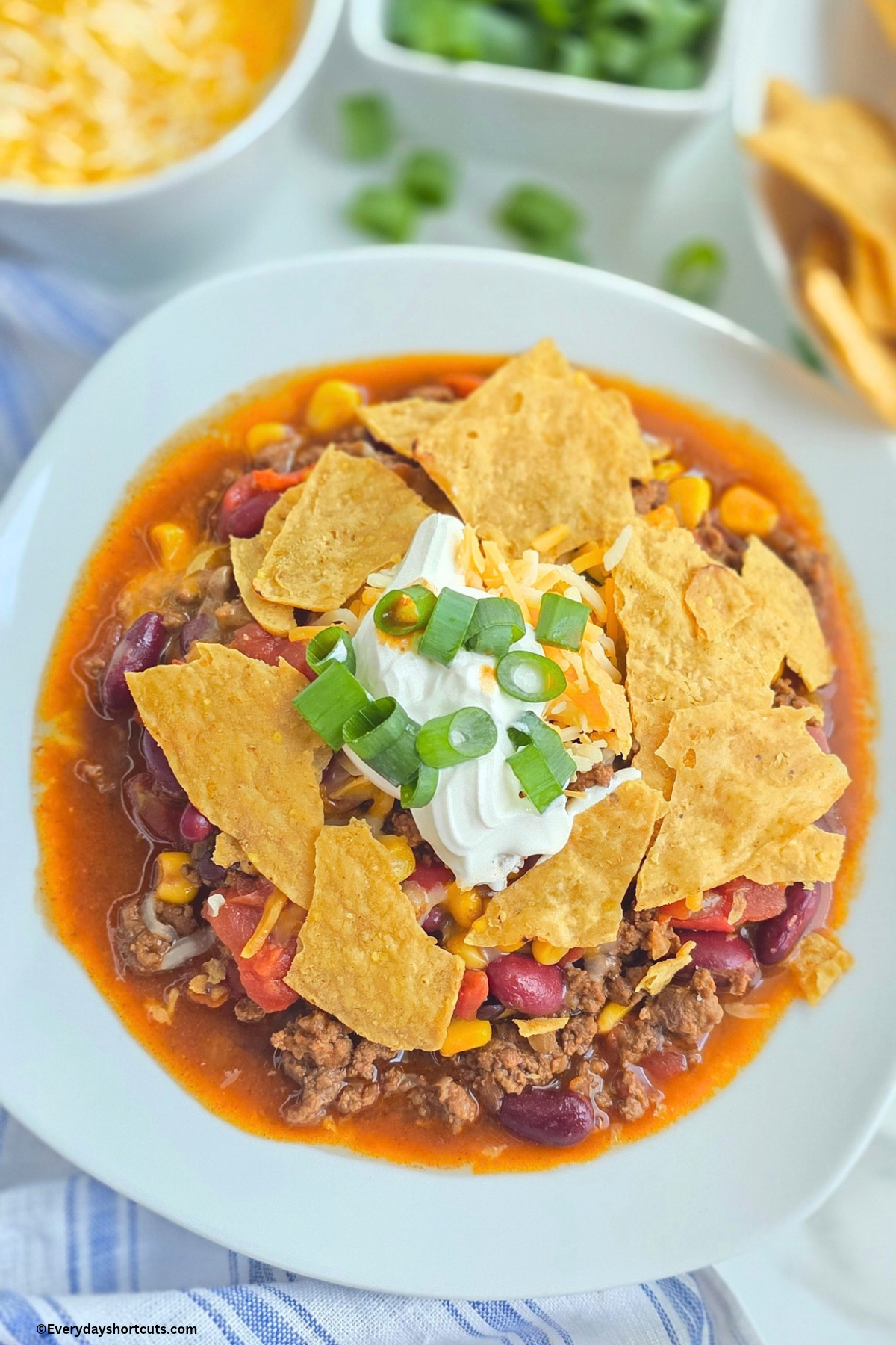 taco soup on a white bowl with crushed tortilla chips on top, shredded cheese, sour cream and green onions