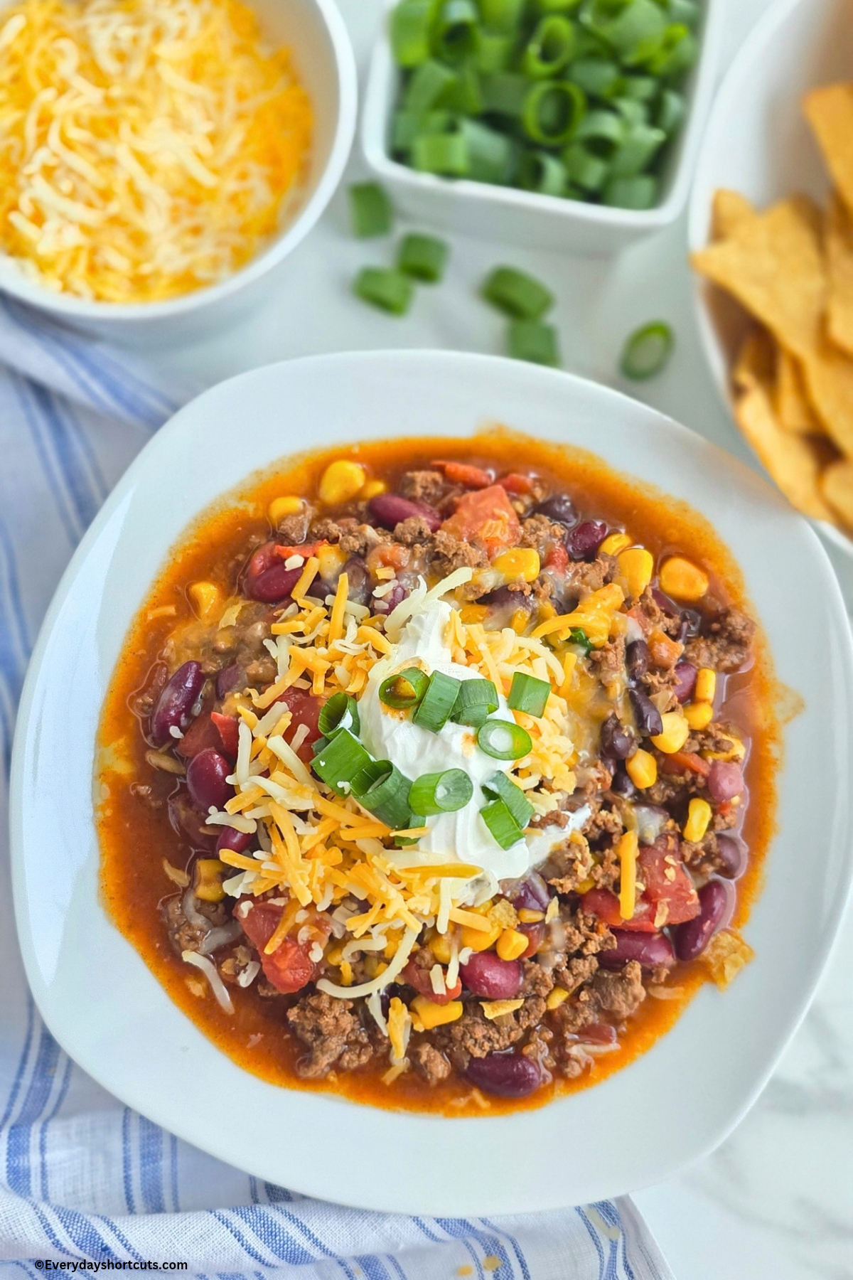 taco soup in a white bowl next to bowls of cheese, green onions and tortilla chips