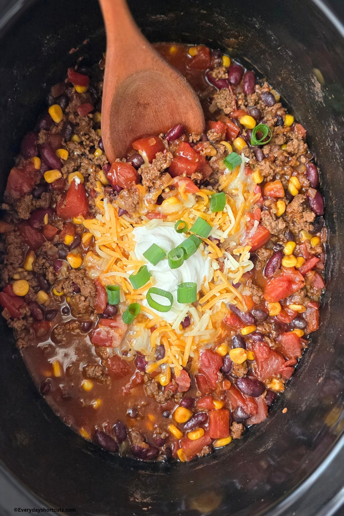 taco soup in a crockpot with cheese, sour cream and green onions on top