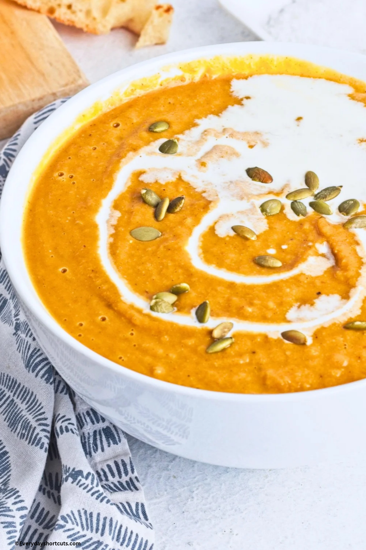 up close bowl of creamy pumpkin soup with heavy cream and pumpkin seeds drizzled on top