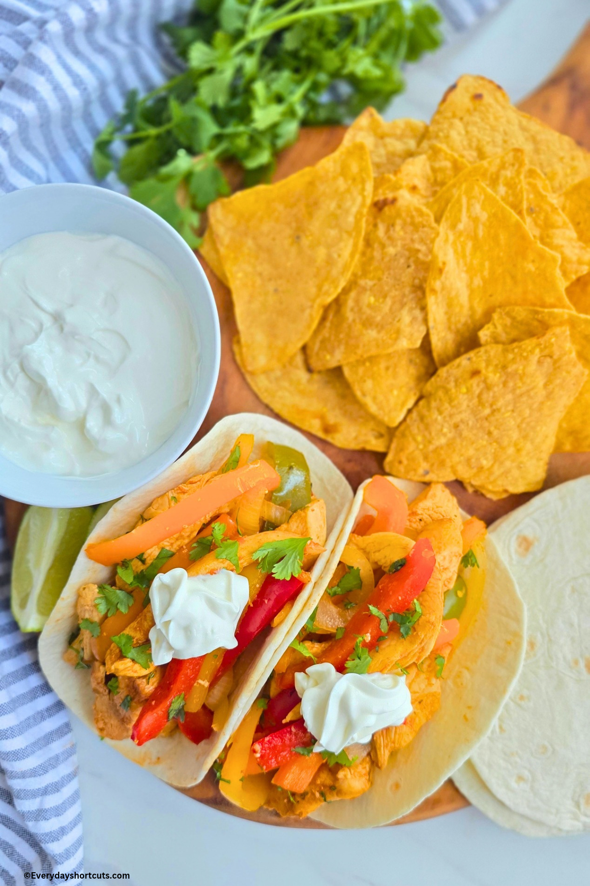 chicken fajitas on a board next to chips, bowl of sour cream and flour tortillas