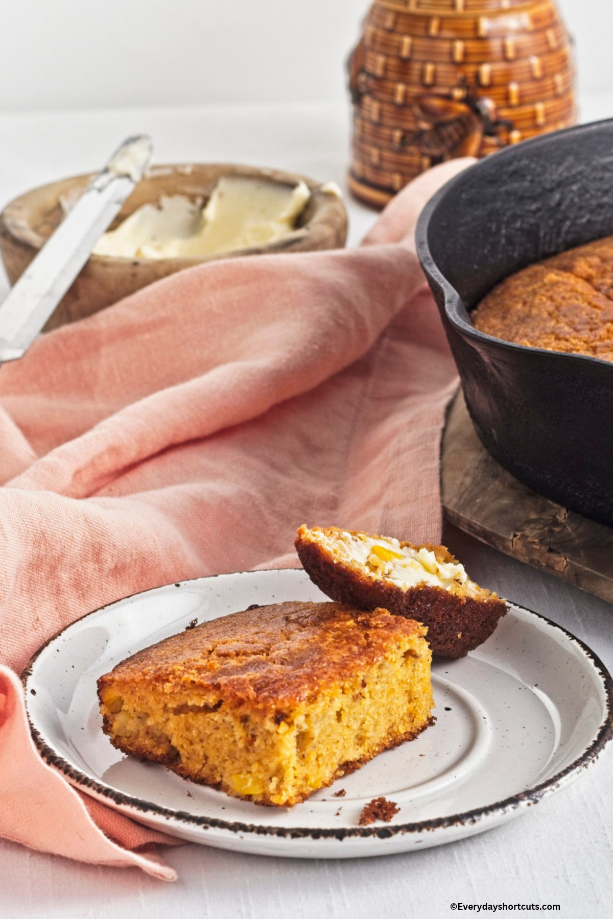 2 slices of cornbread on a white plate next to a reddish pink napkin