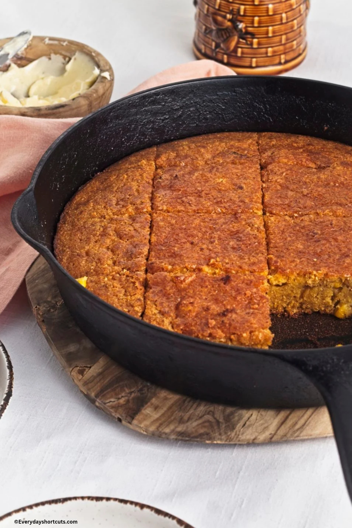 up close of cut corn bread in a cast iron skillet next to a bowl of butter