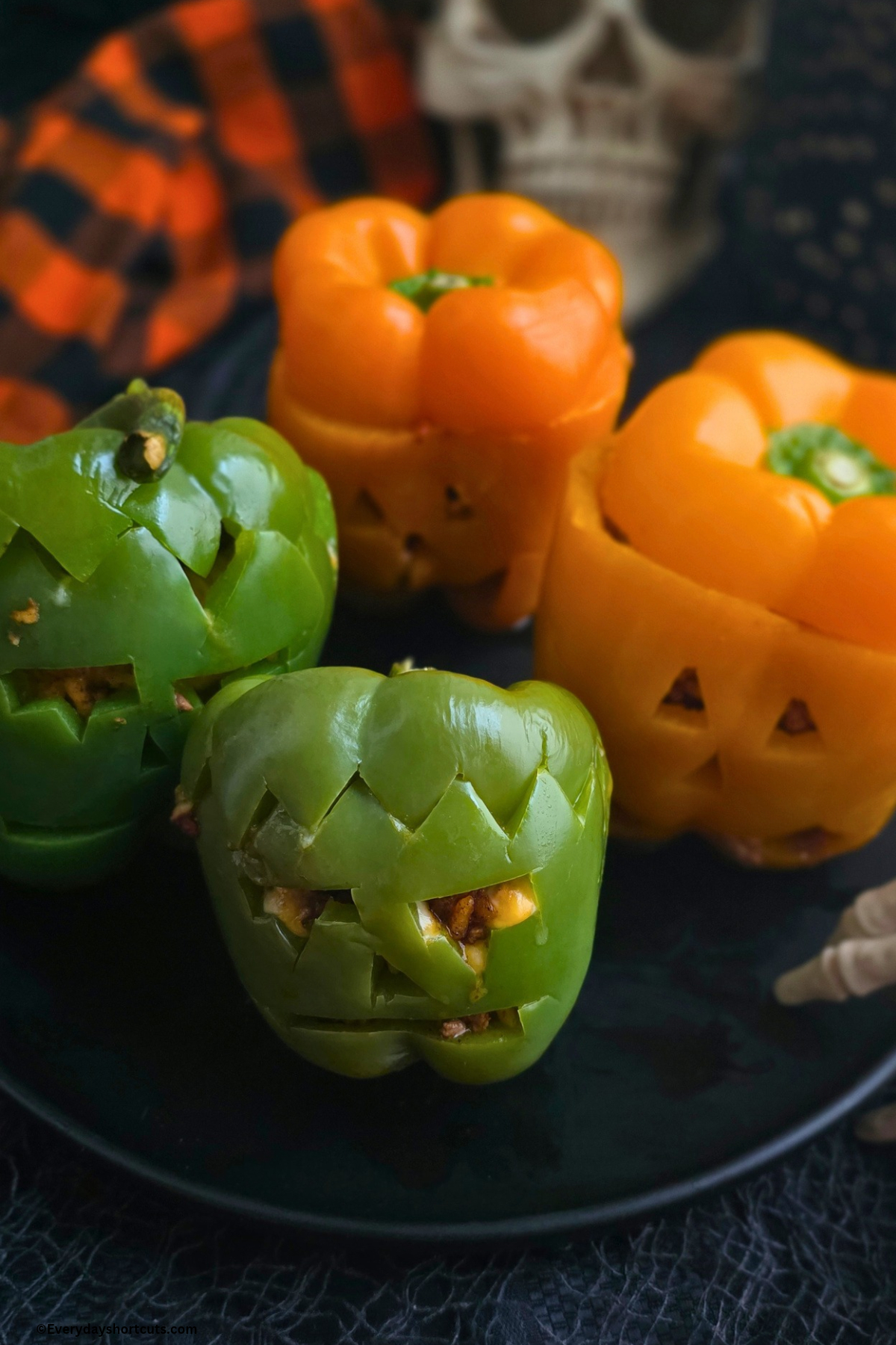 Halloween stuffed peppers on a black plate next to a plastic skull