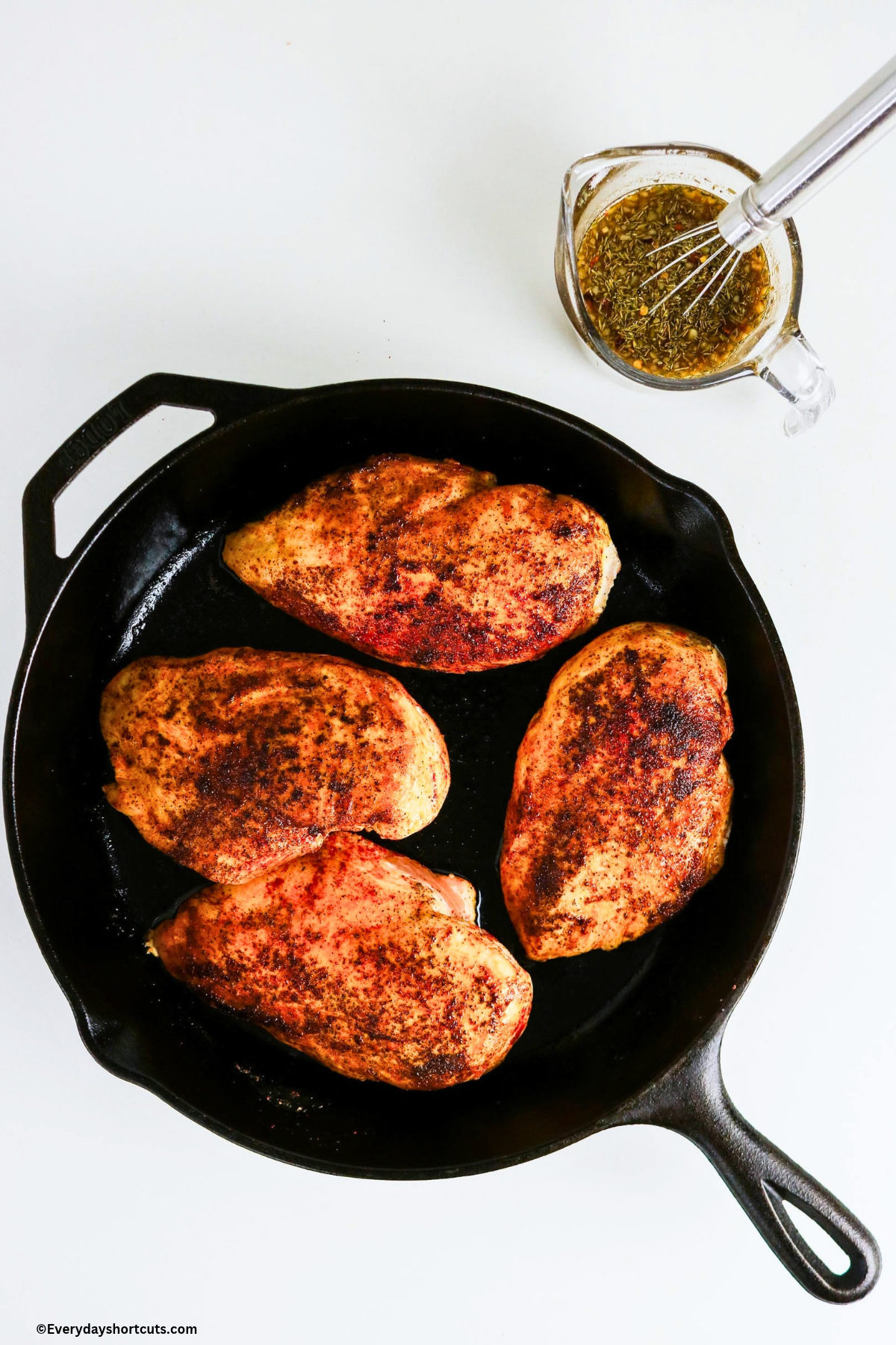 cooked chicken breasts in a cast iron skillet next to a measuring cup of the mustard glaze