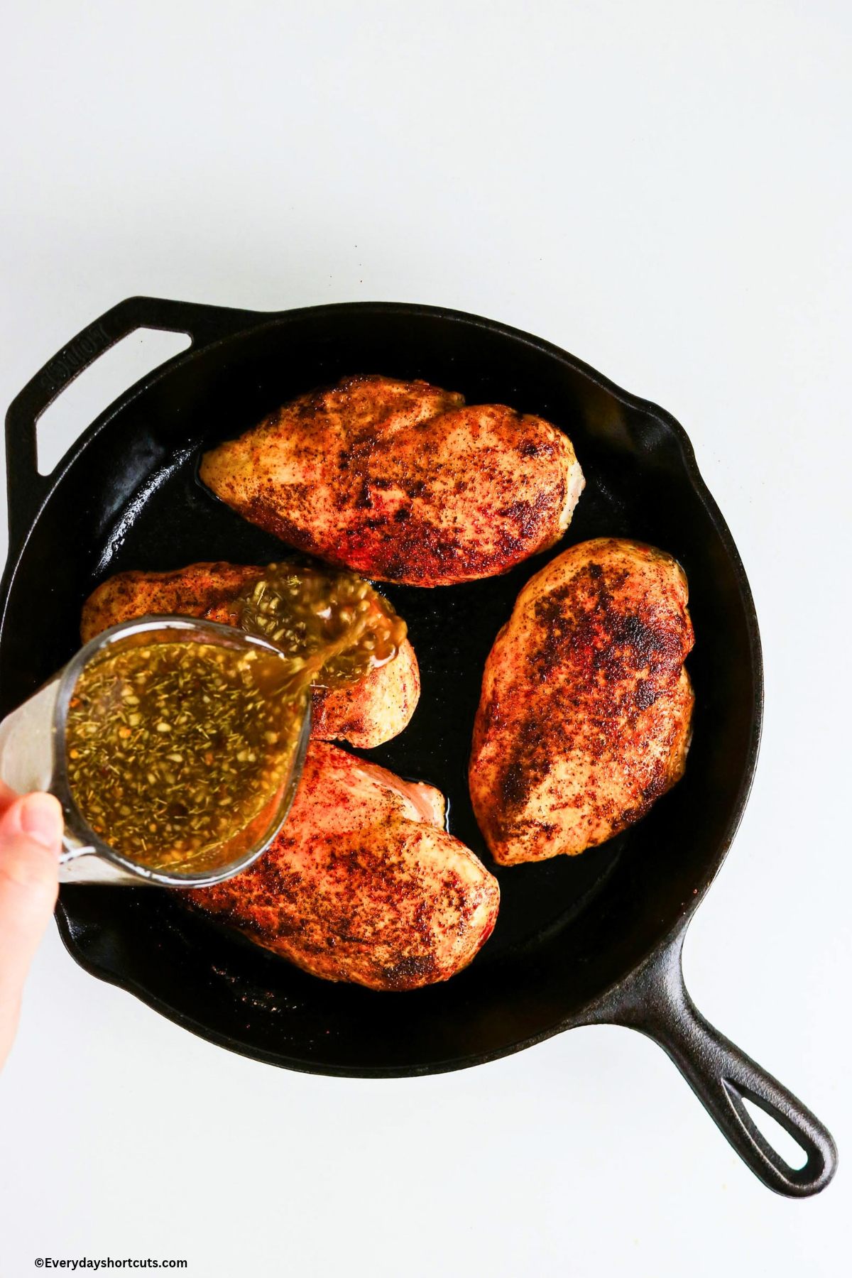 pouring maple dijon glaze over chicken breasts in a cast iron skillet