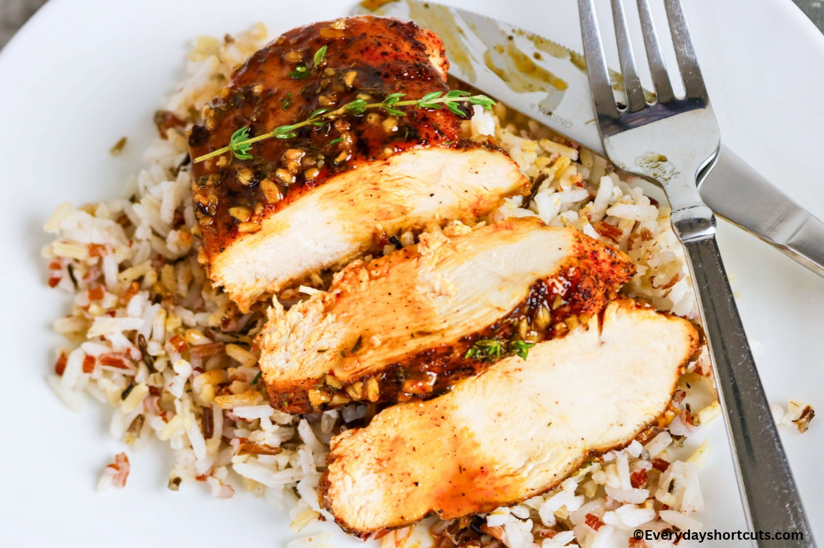 sliced maple dijon chicken on a white plate on top of a bed of rice and next to a knife and fork